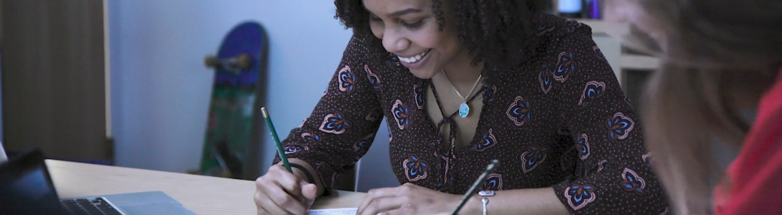 A young woman designer smiles while writing at the Loyola College of Music and Media.
