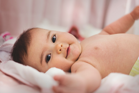 Photo of a baby lying on a blanket, looking at the camera.