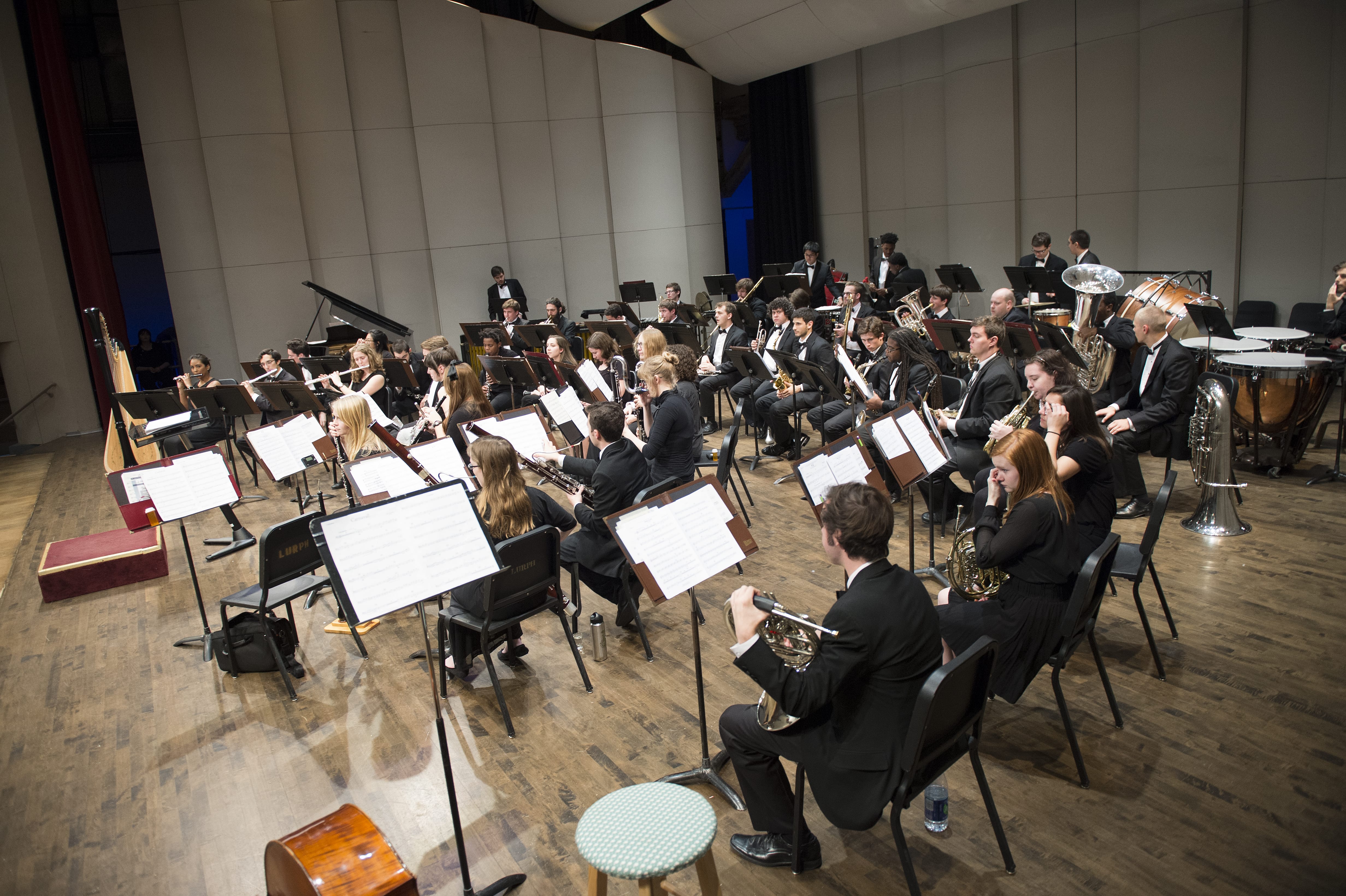 A wide shot of a large Loyola band warming up on stage in concert dress.