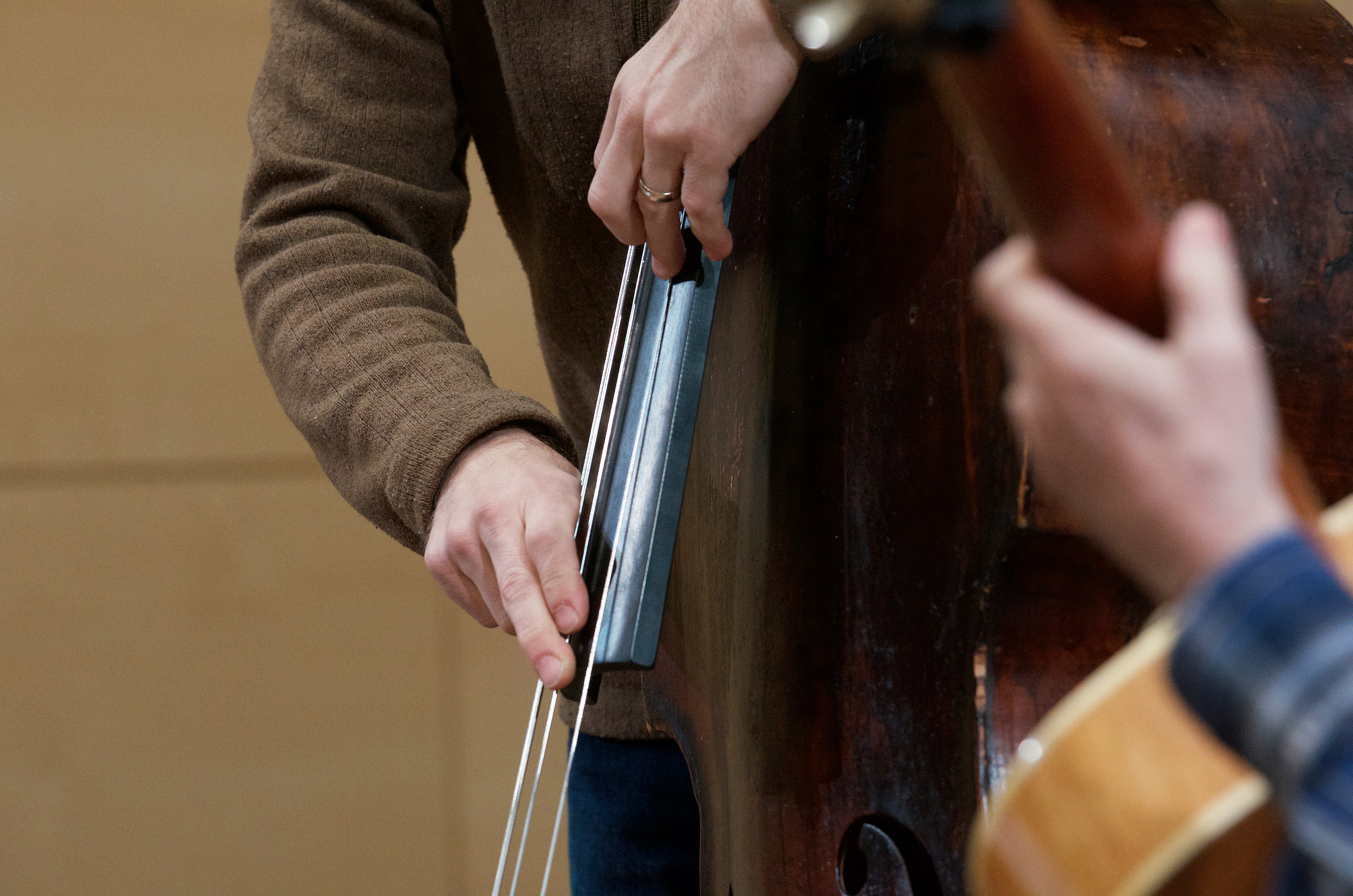 A close up of a jazz bass player plucking their instrument, with an out of focus guitar in the foreground.