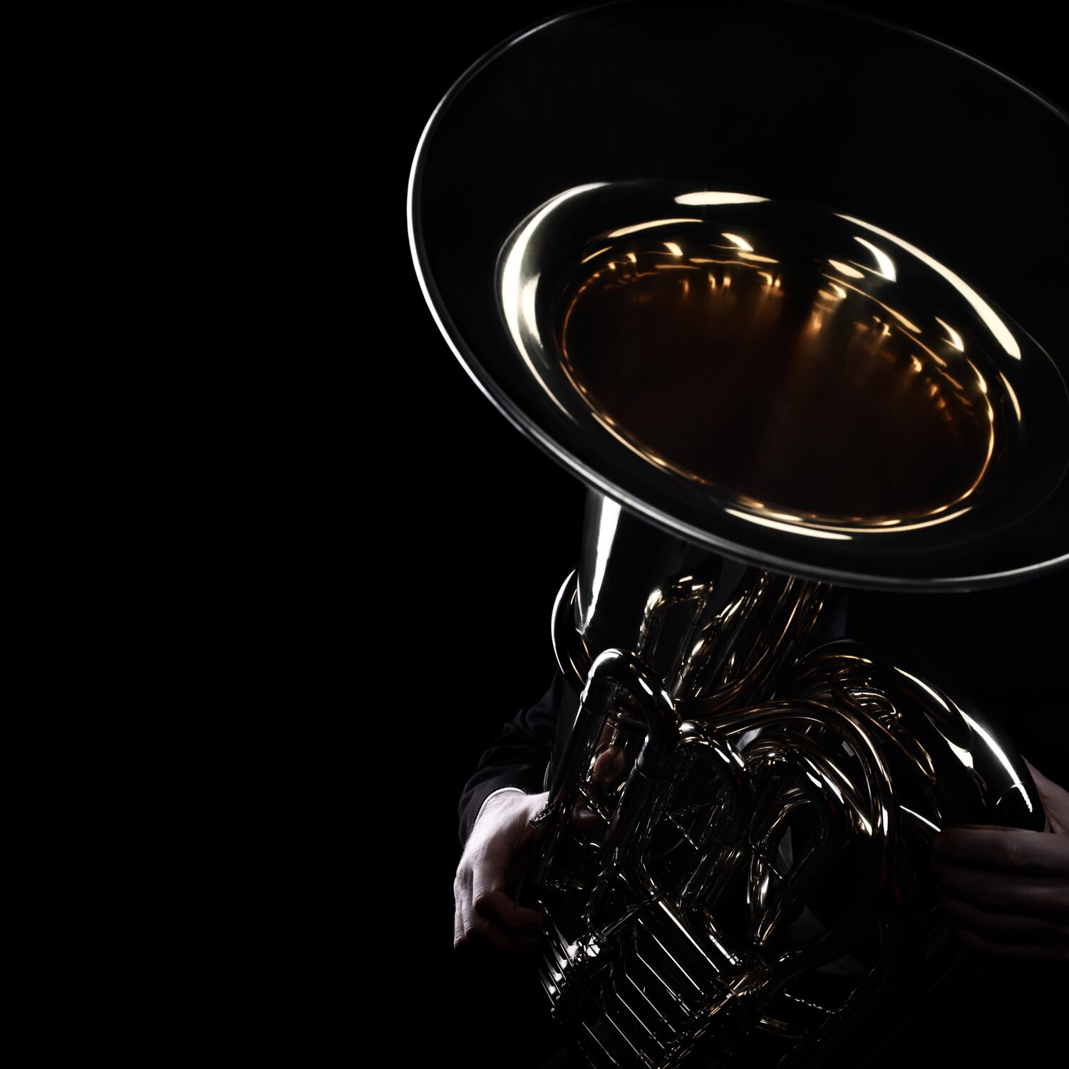 A dark silhouette of a tuba player against a black backdrop.