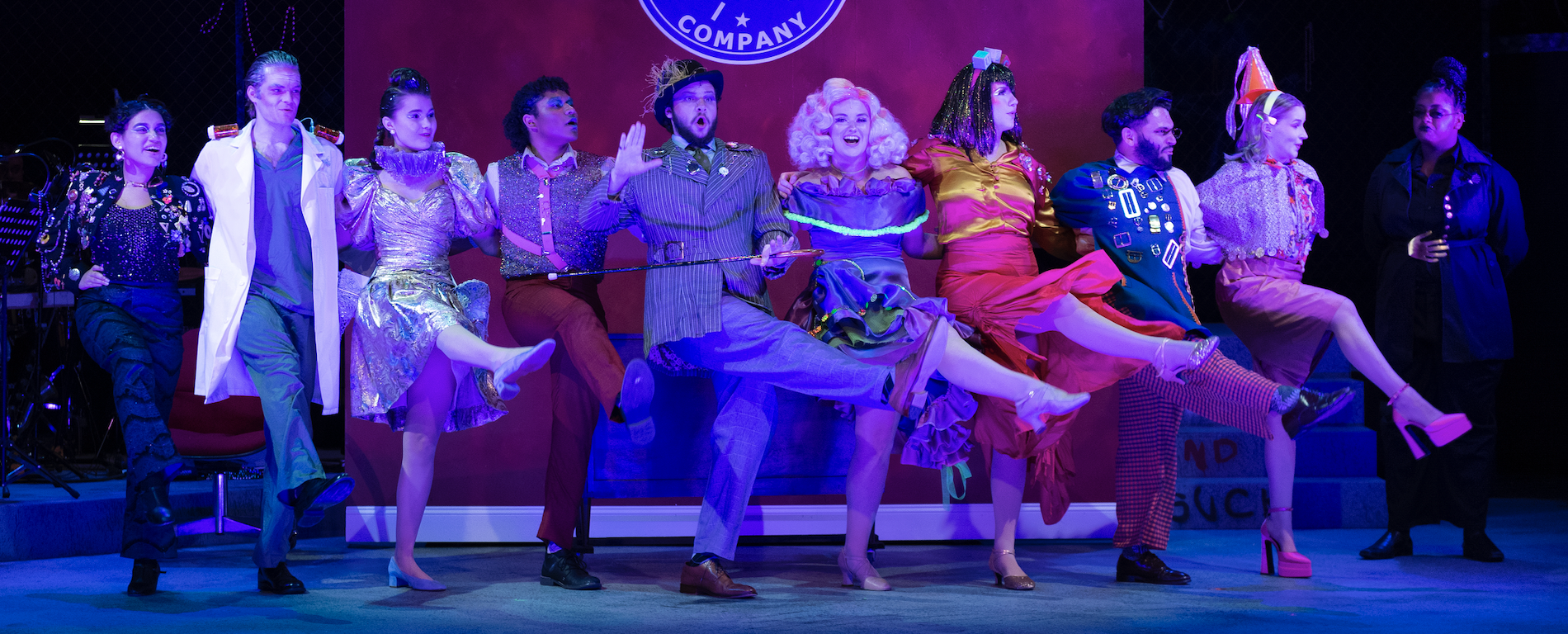 A group of people kick up with one leg in a dance number from the musical URINETOWN